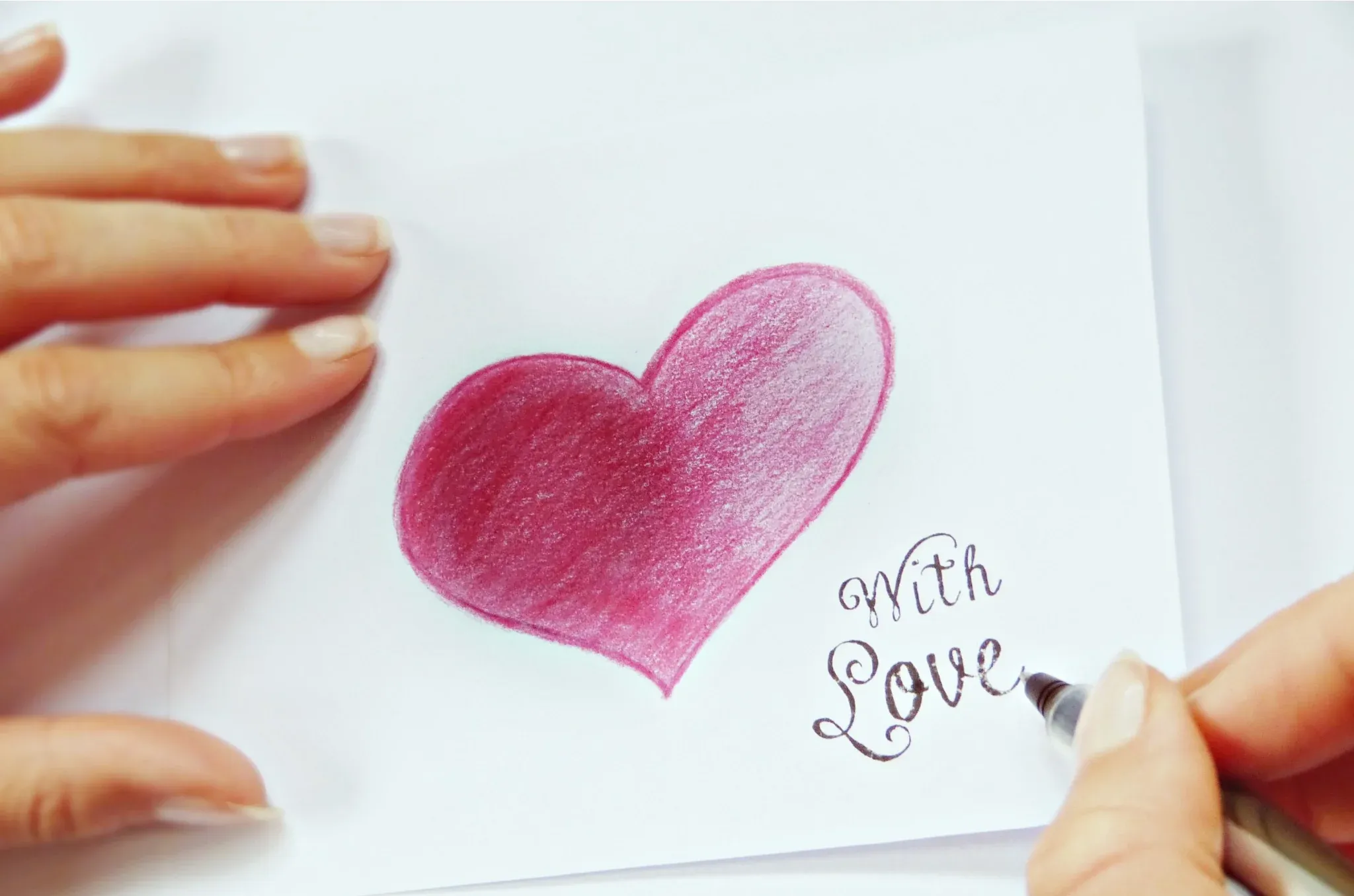 白い紙にピンクのハートと「with Love」を書く手。
