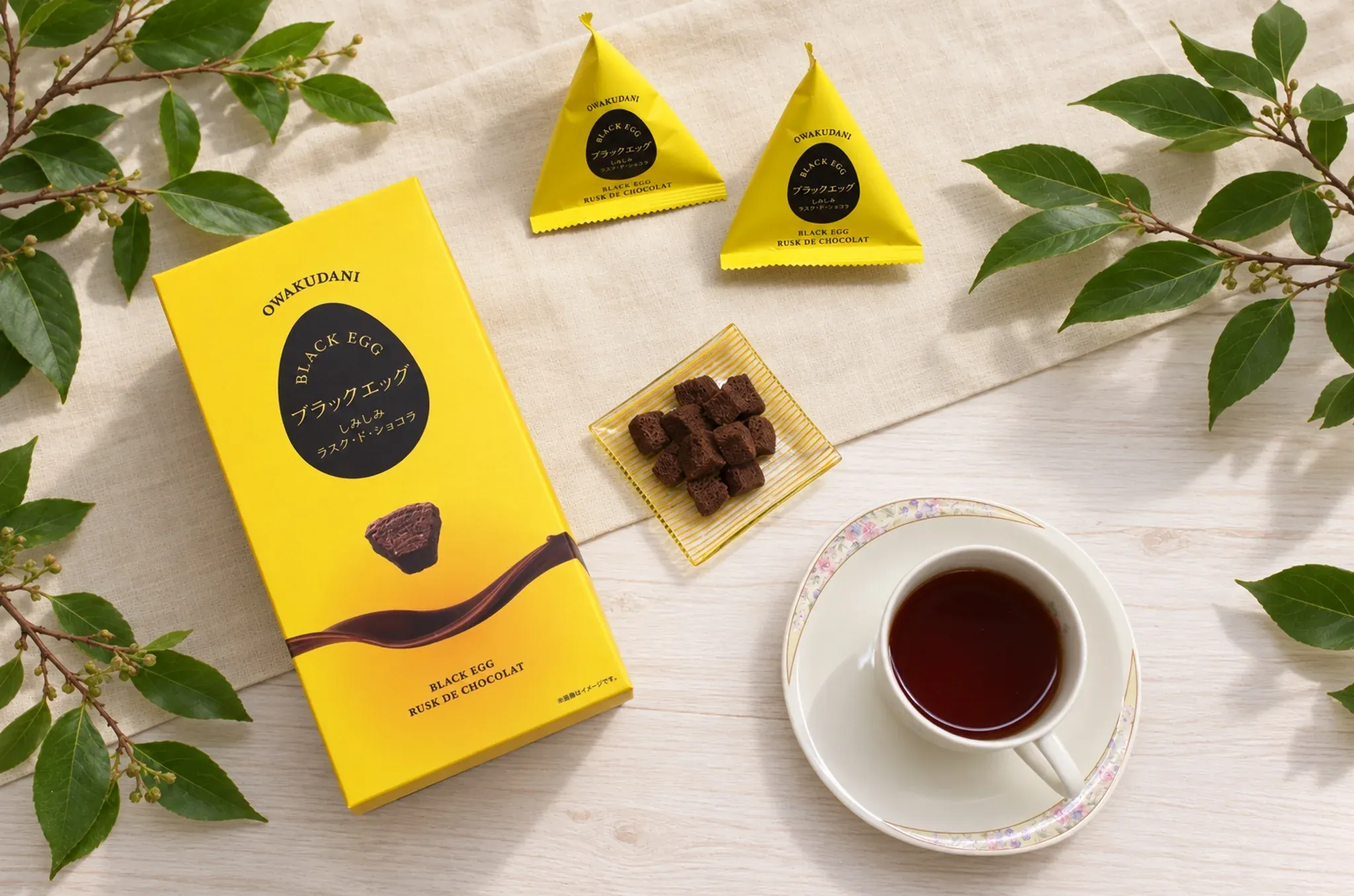 Box and triangular packs of Black Egg Shimishimi Rusk de Chocolat beside tea.