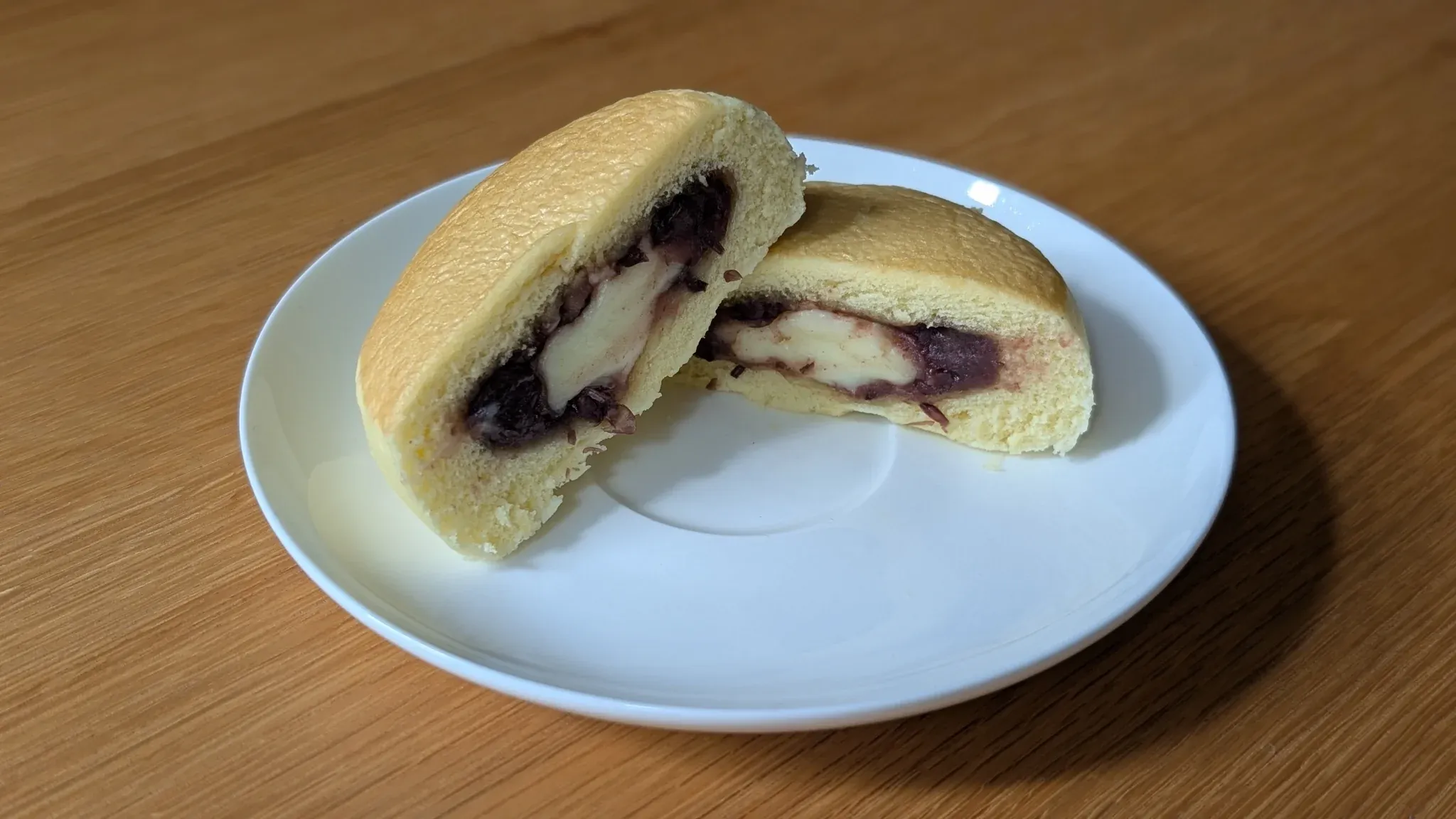 白い皿の上で半分に切られたホットケーキまん。中にはあんことバタークリームの層が見える。