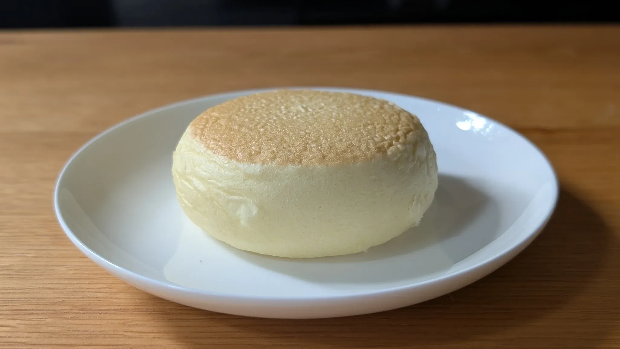 白い皿の上に、きつね色の表面を持つ丸いホットケーキまんが一つ置かれている。木のテーブルの上に並ぶ。
