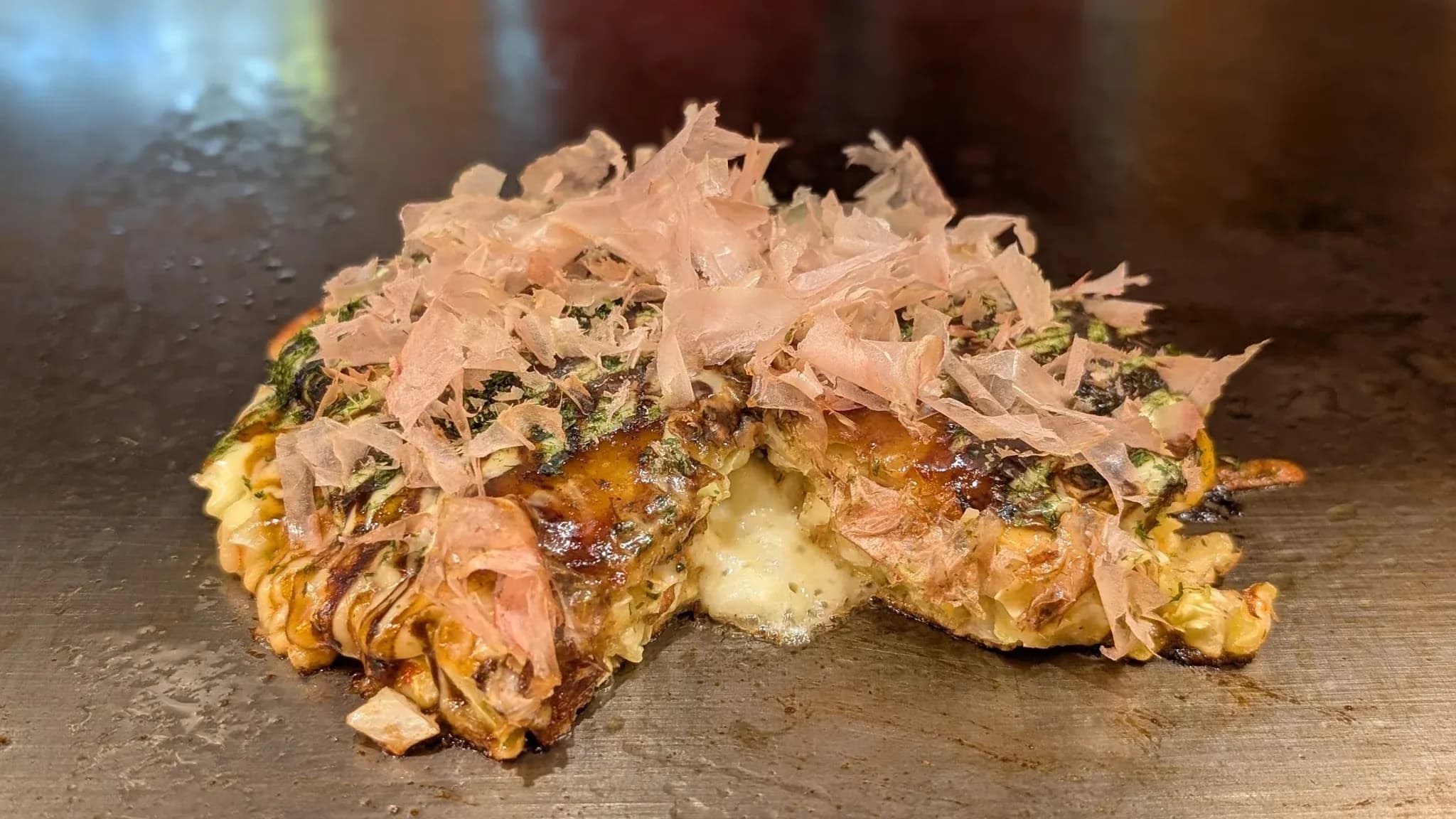 中のチーズがとろけるように見える、かつお節をのせたお好み焼き。