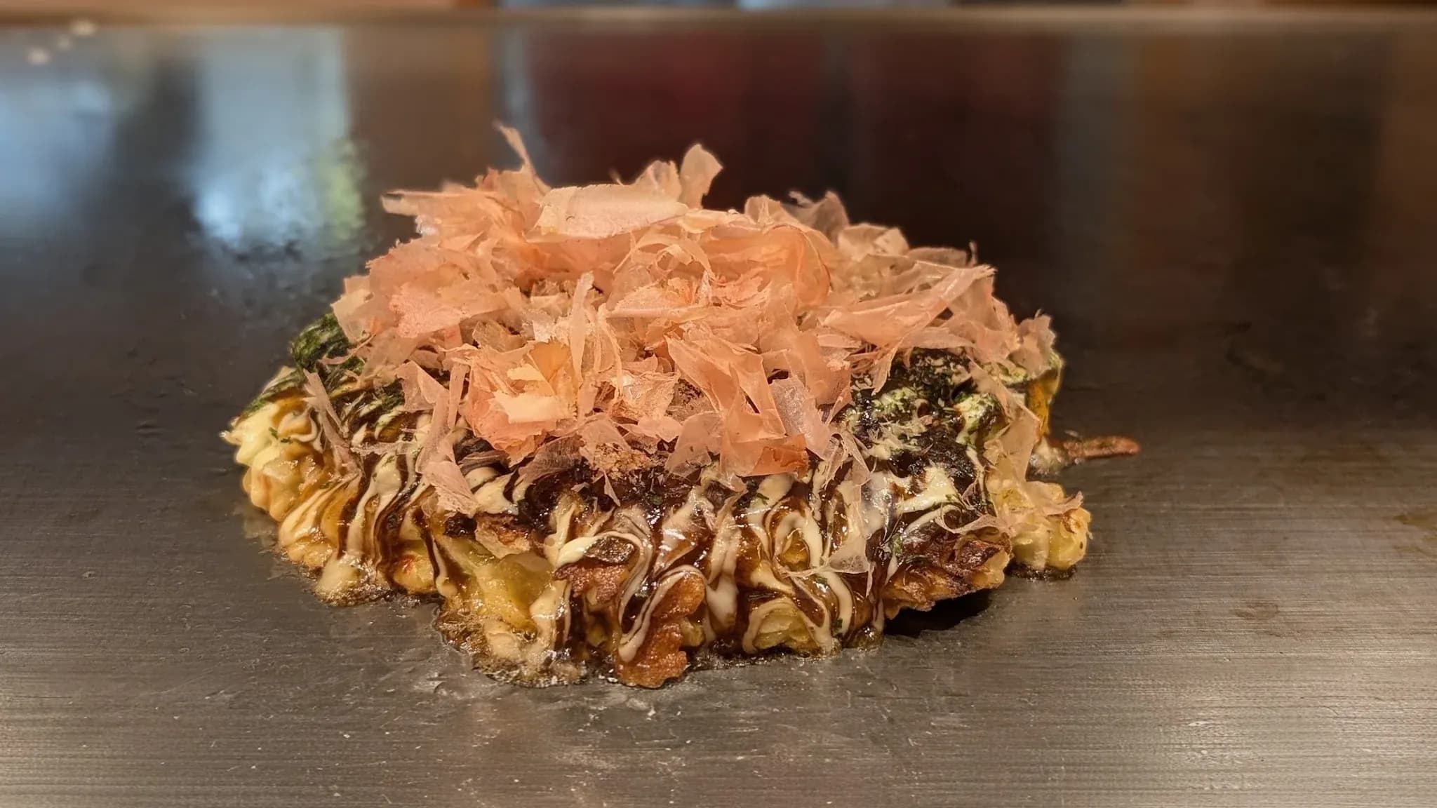 鉄板の上に焼きたてのお好み焼き。上にはかつお節がのっている。