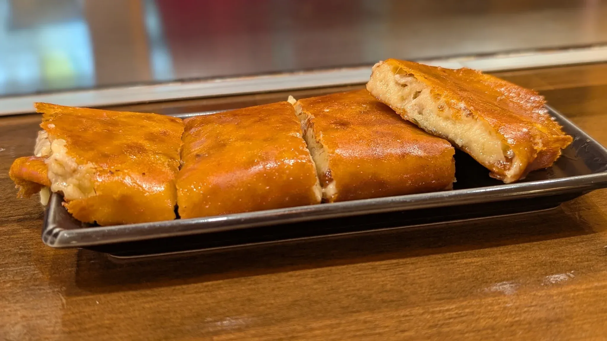 焼き色のついたポテトサラダが並ぶ長方形の皿。ひと切れが持ち上げられ、中のやわらかい部分が見えている。